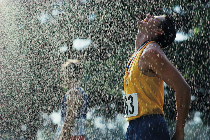 ゴールラインを通過した後の男性アスリート。 雨が降っている。 落ちてくる雫に頭を上に向けている。 目を閉じ、首にメダルをかけている。 ゼッケン63の黄色いタンクトップに青い短パン。