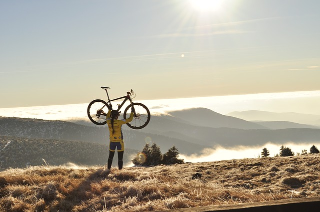 自転車を頭上に掲げるサイクリスト。 背景は霧に包まれた山々。