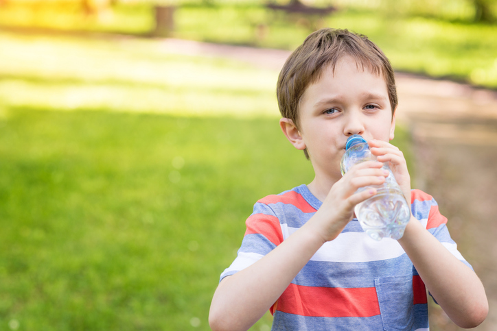 ボトルから水を飲む少年、背景は緑の芝生