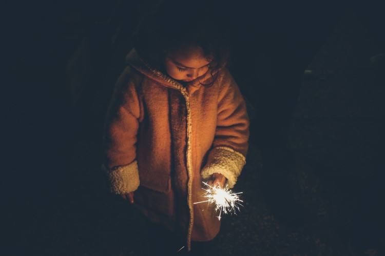 コートを着て線香花火を手にした少女が、悲しそうに地面を見ている。