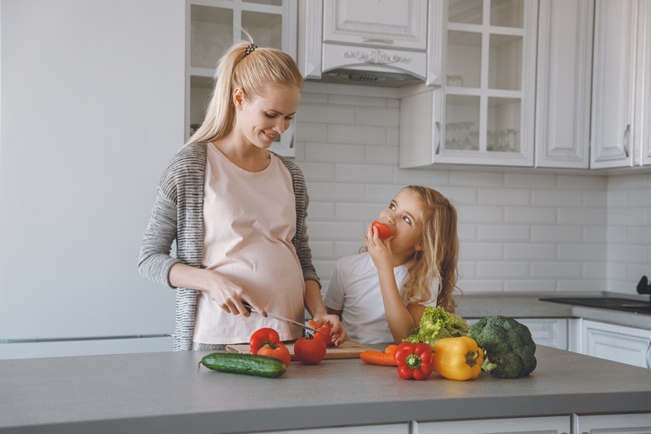 キッチンで健康的な食事を準備する妊娠中の母親と娘。