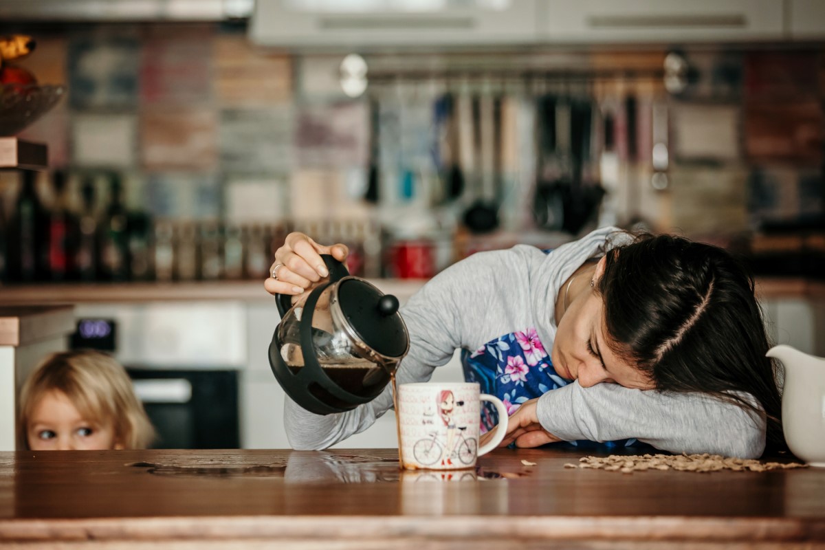 疲れた女性がキッチンカウンターに横たわり、マグカップの横でコーヒーをこぼしている。