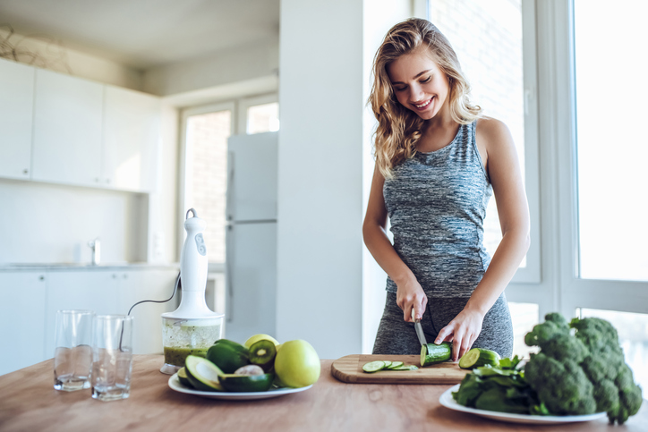 若い女性がキッチンで野菜を切っている。