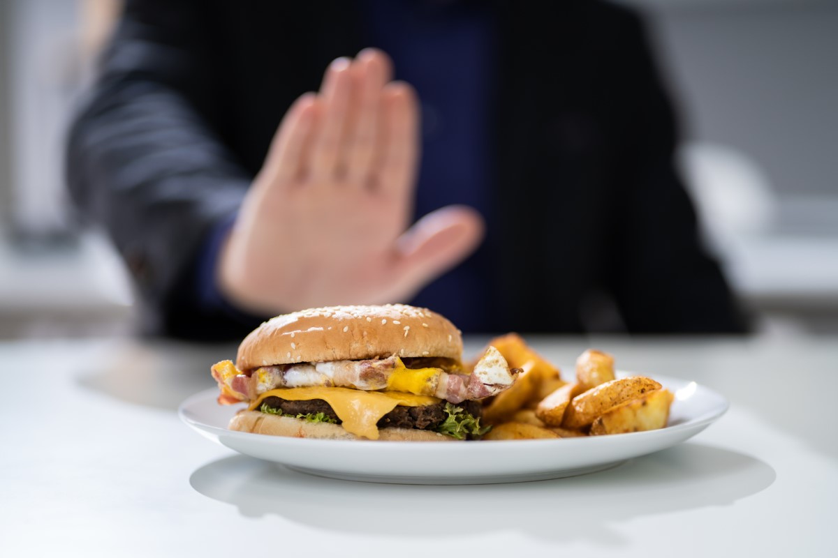 胸焼けの原因として不適切な食べ物-男性が拒否した皿の上のハンバーガー